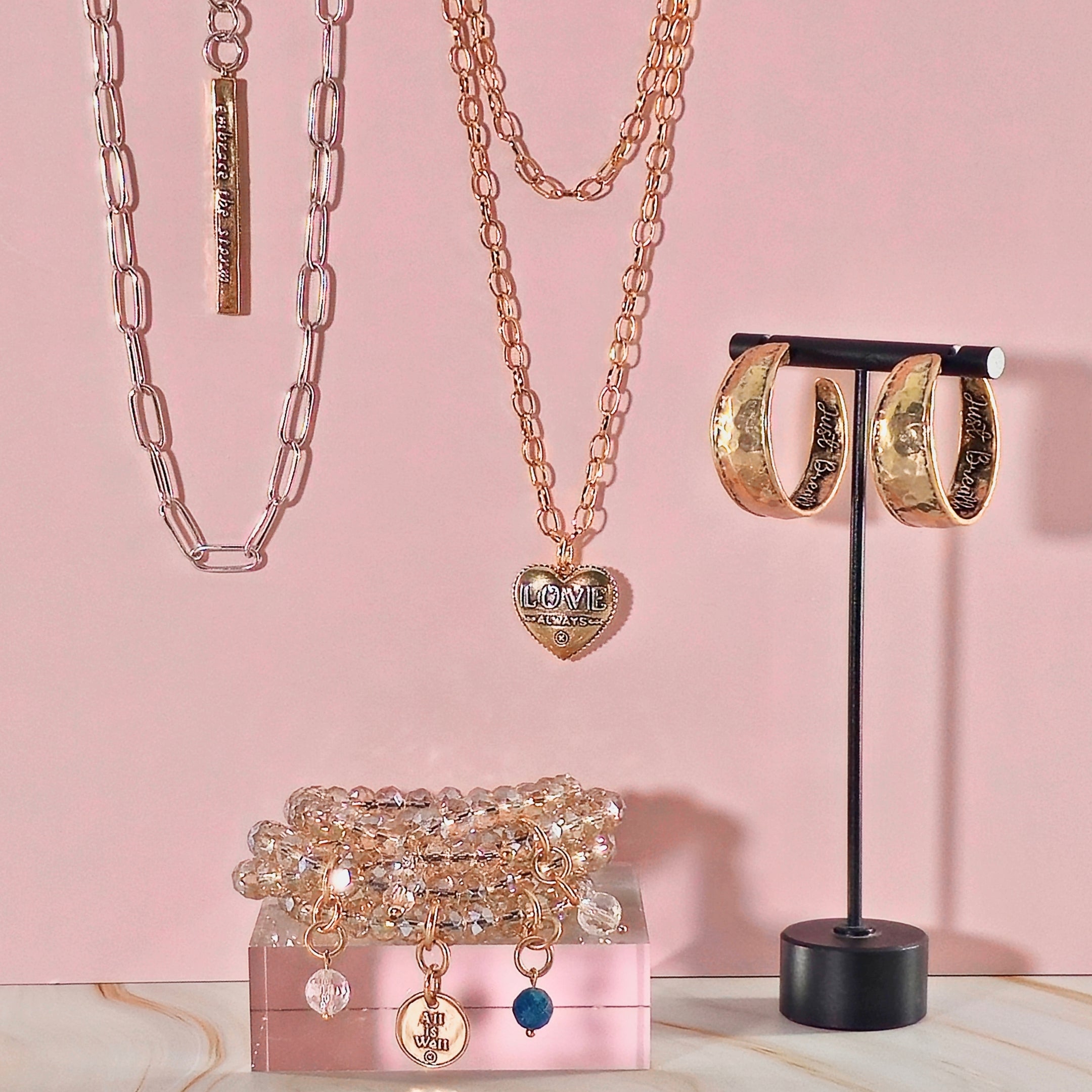 Jewelry set including necklaces, bracelets, and hoop earrings on a pink background