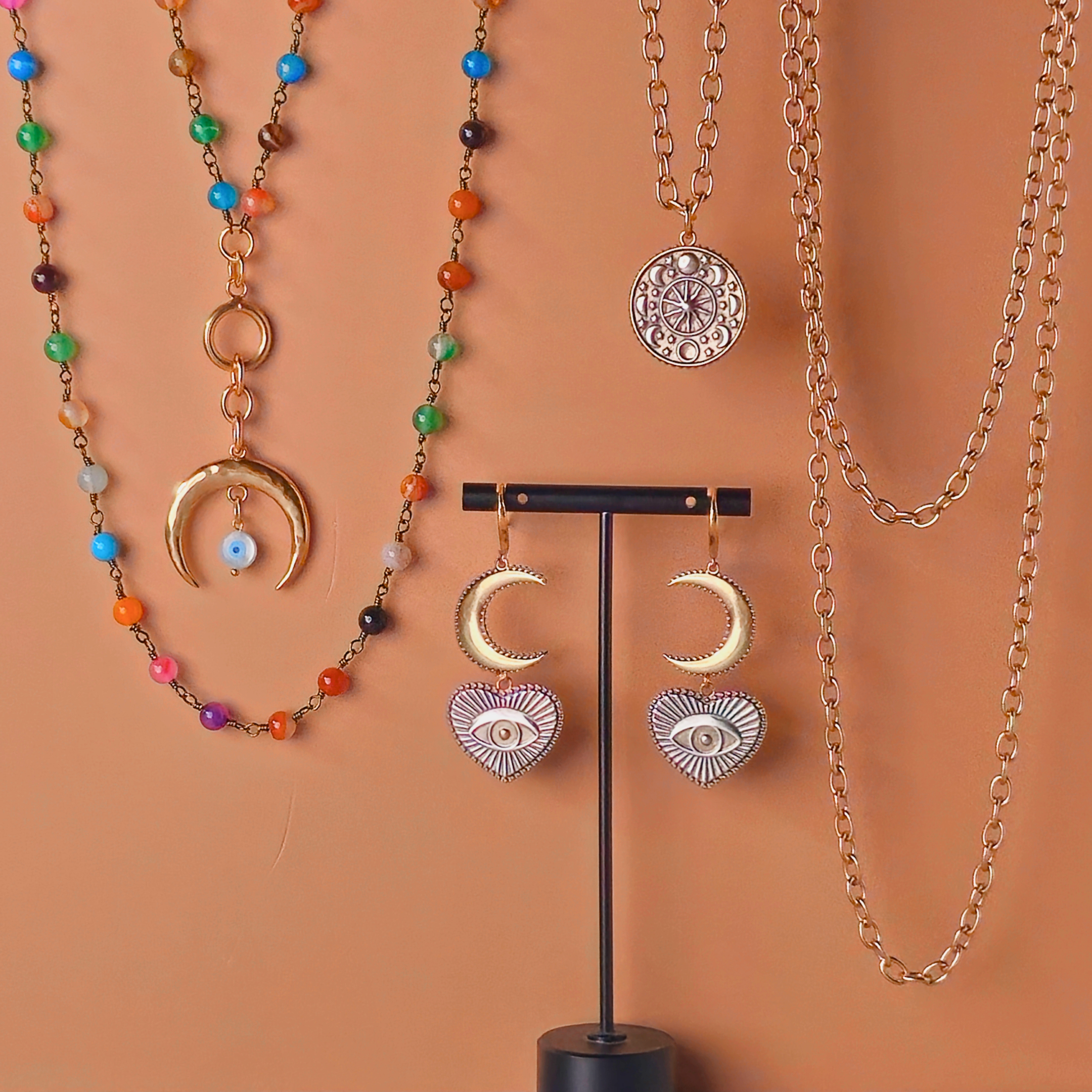 Jewelry set with necklaces and earrings on a stand against an orange background