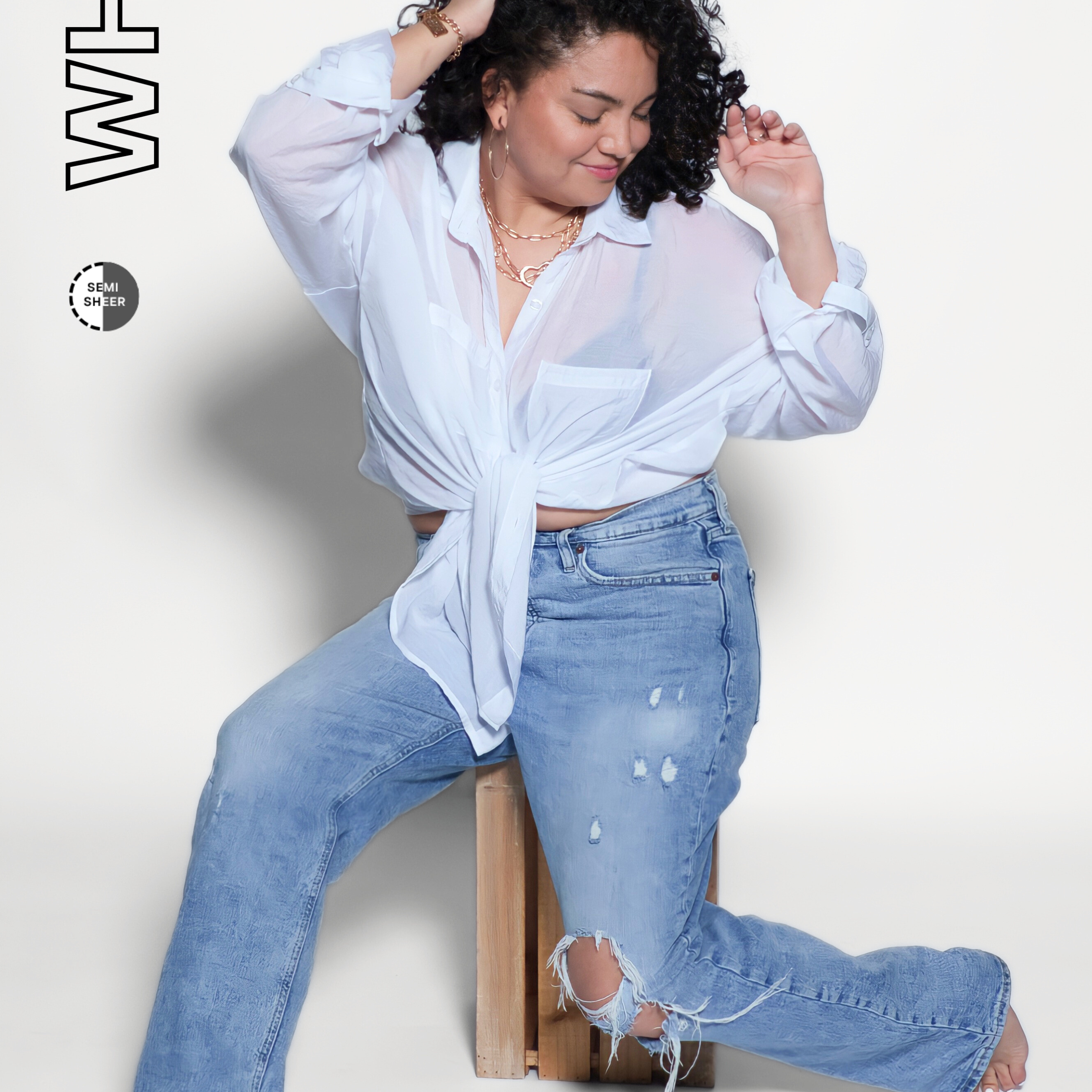Woman wearing a white shirt and blue jeans sitting on a wooden block against a white background.