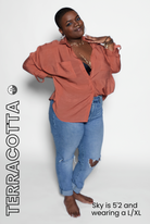 Woman wearing a terracotta blouse and blue jeans on a white background