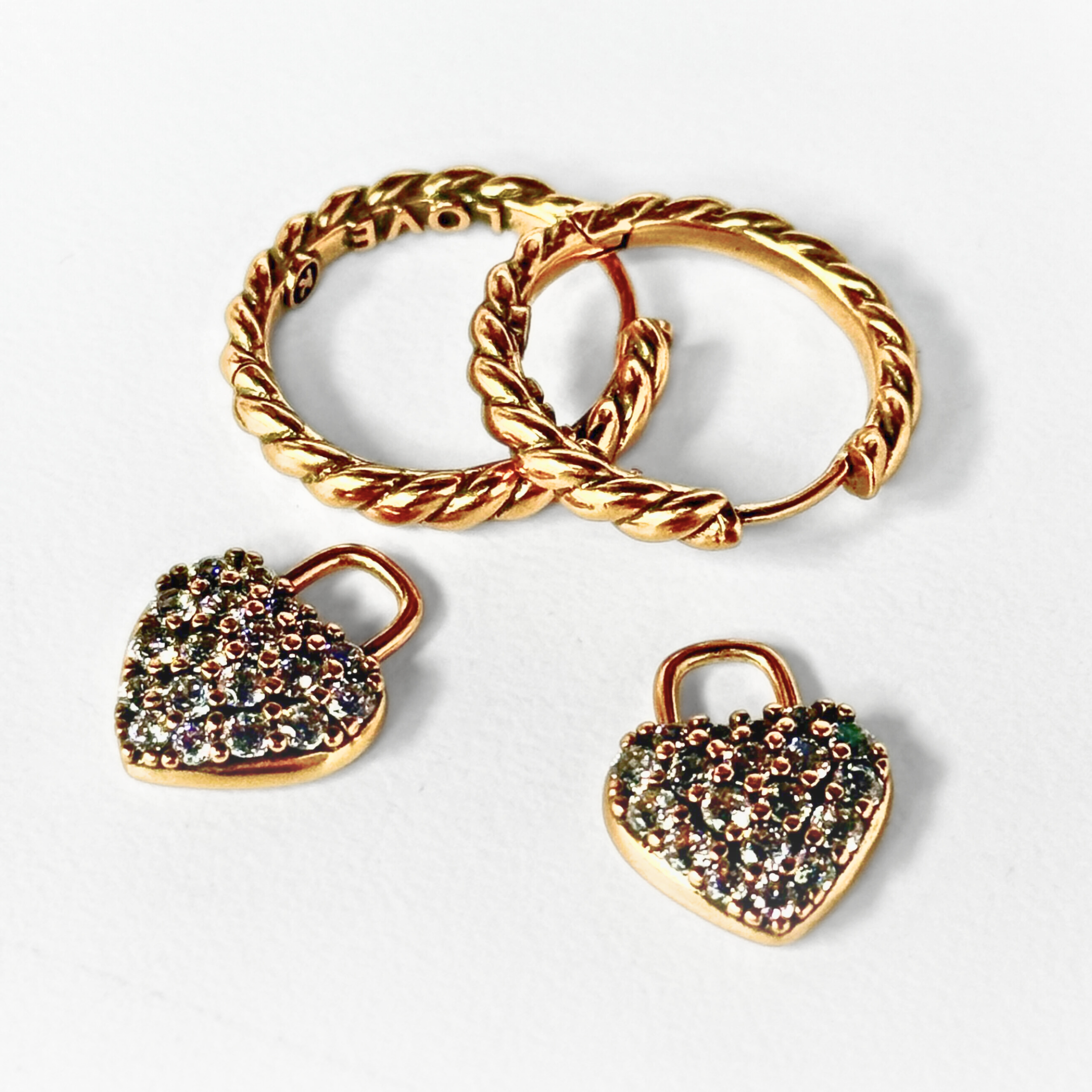 Gold hoop earrings with heart-shaped padlock charms on a light gray background