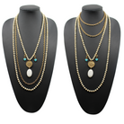 A person wearing a black shirt and showcasing a long gold chain necklace with off-white and blue howlite stones, along with matching bracelets and earrings.