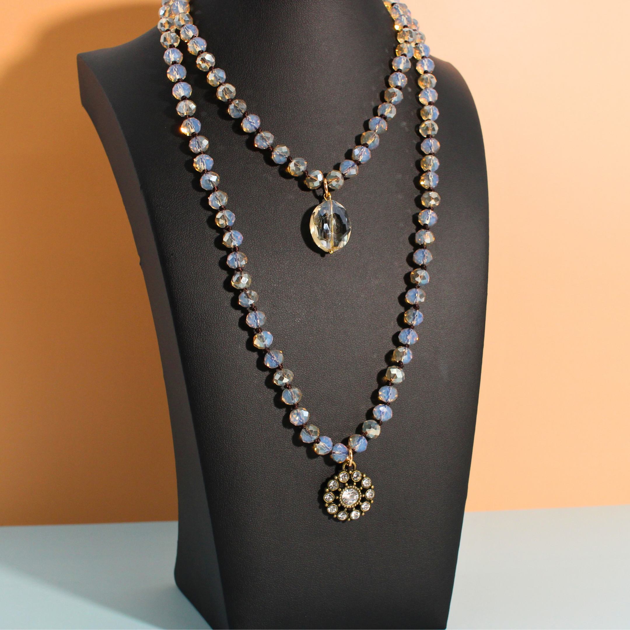 Necklace with two pendants on a black mannequin against a peach background