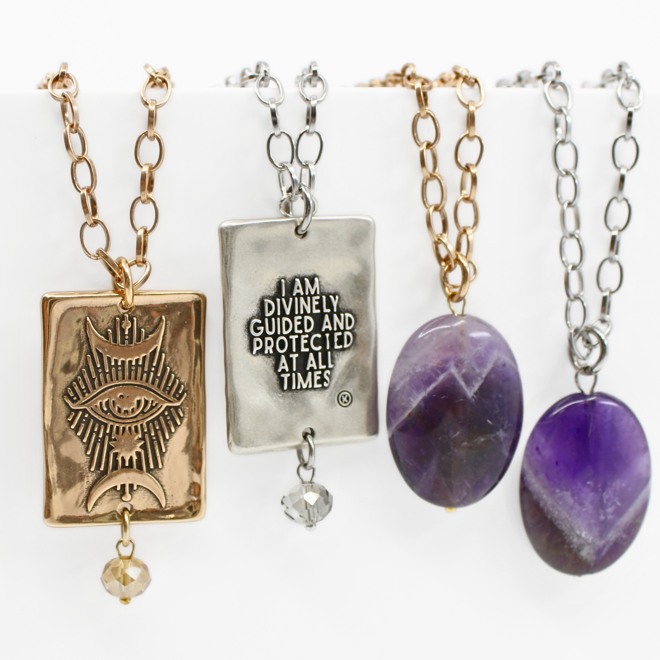 Three necklaces with silver chains and gold-tone pendants. One pendant has a geometric design, another features a square with text, and the third displays a heart shape.