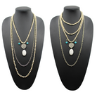 A person wearing a black shirt and showcasing a long gold chain necklace with off-white and blue howlite stones, along with matching bracelets and earrings.