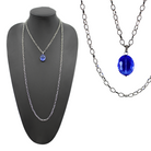 Two chain necklaces, one with a silver finish and the other with an antique gold finish, each featuring a large faceted royal blue crystal.