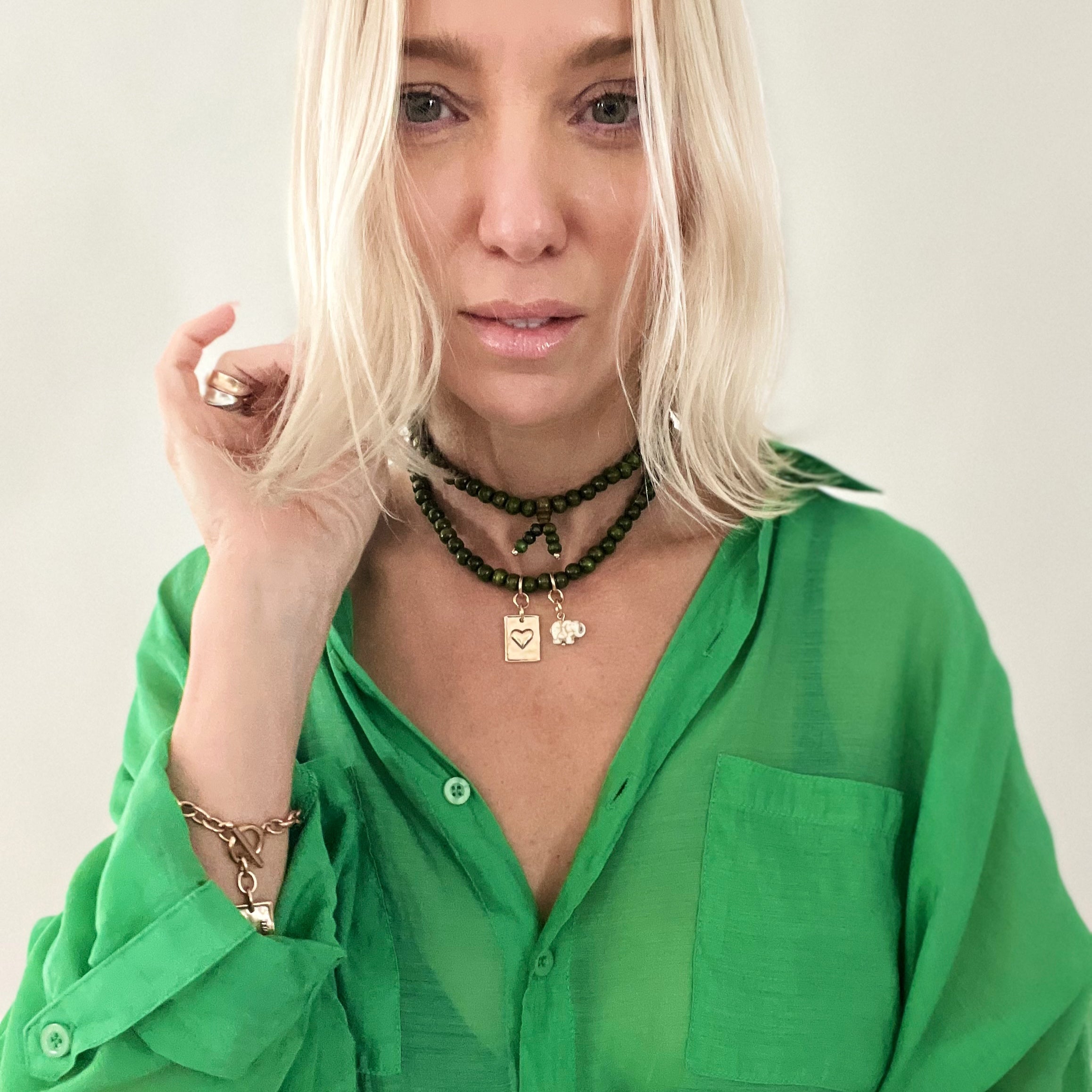 A person wearing a green shirt and showcasing a wooden boho wrap bracelet with a gold finish pendant and an off-white howlite elephant charm.