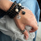 A person's wrist wearing a black wooden Boho wrap bracelet with a silver finish pendant and river stone accents.