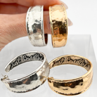A pair of hoop earrings with a hammered texture in silver and gold colors, featuring the inscription 'JUST BREATHE' on the silver earrings, and 'I JUST BREATHE' on the gold earrings.