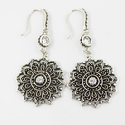 Pair of silver mandala-style earrings with clear stones on a white background