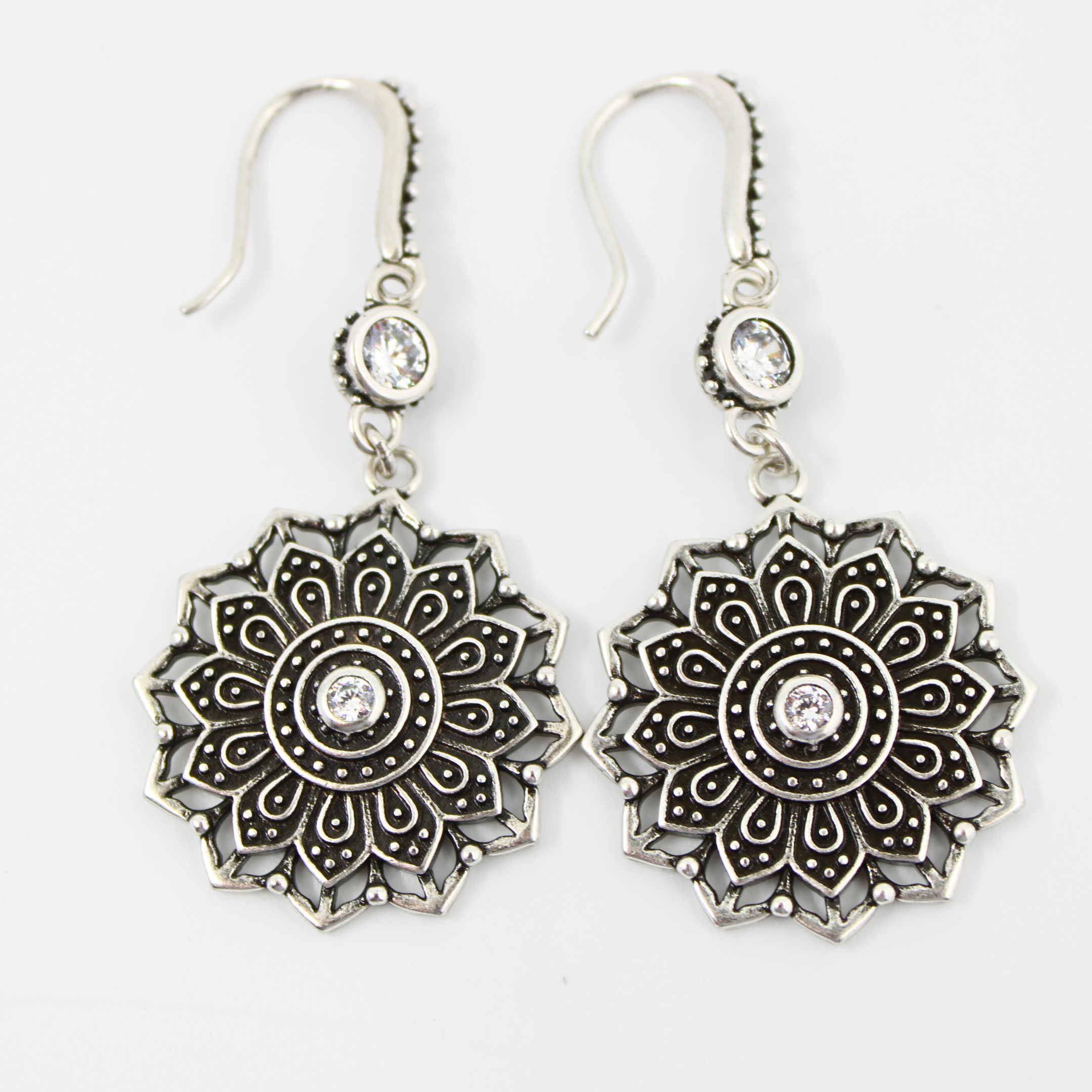 Pair of silver mandala-style earrings with clear stones on a white background