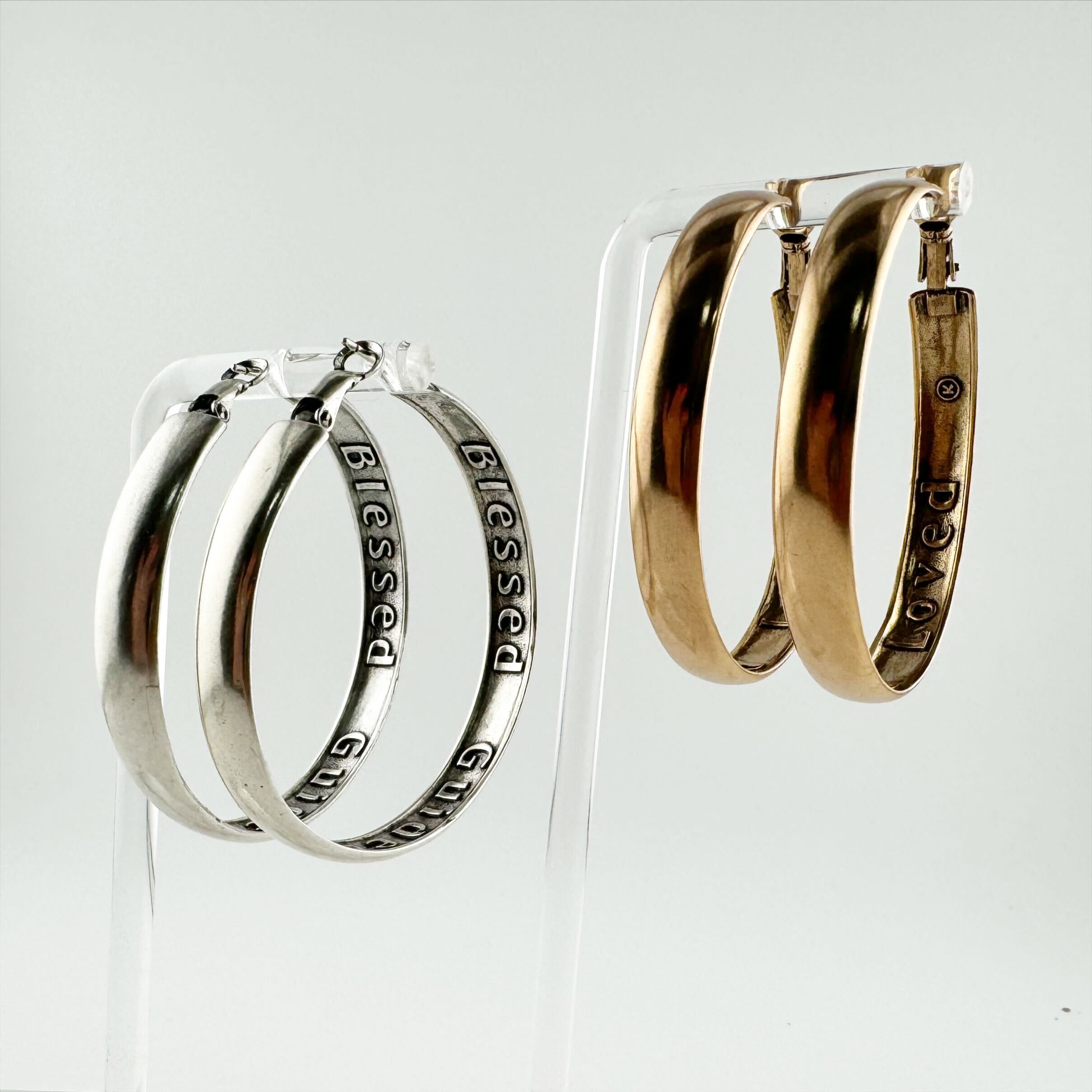 A pair of hoop earrings with 'BLESSED GUIDED LOVED' inscribed on the inside, one pair in silver and the other in gold color, displayed against a white background.