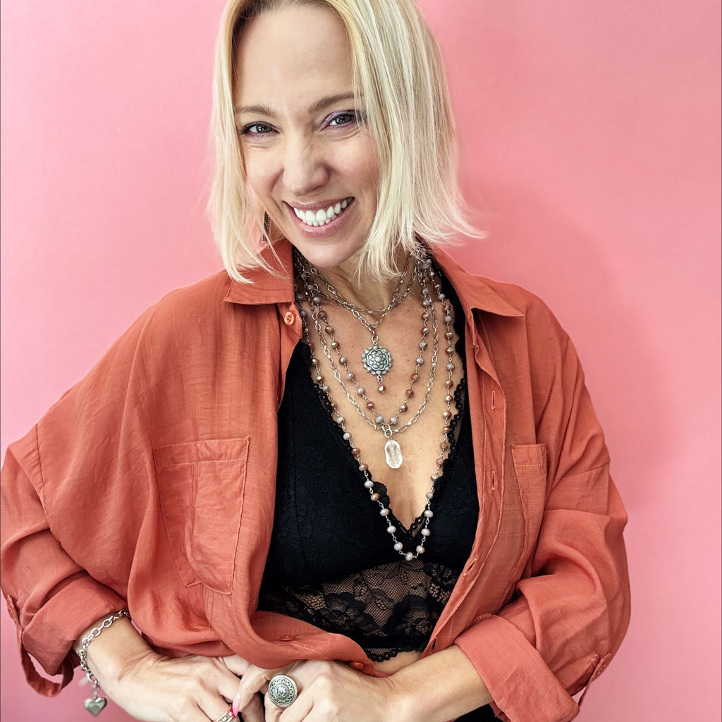 A stylish multi-layered necklace featuring delicate rosary-style chains adorned with small beads and intricate silver accents. The necklace includes multiple strands of varying lengths, with the longest featuring a teardrop-shaped pendant. The design combines bohemian and vintage aesthetics, complementing the wearer's black lace top and earthy-toned outfit.