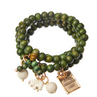 A green wooden boho wrap bracelet with gold finish pendant and off-white howlite elephant charm, displayed on a white background.