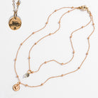 Two dainty necklaces with pendants, one with a silver finish and the other with a gold finish. Both have a chain link design and feature a circular pendant with the phrase 'I am enough' and a heart symbol respectively.