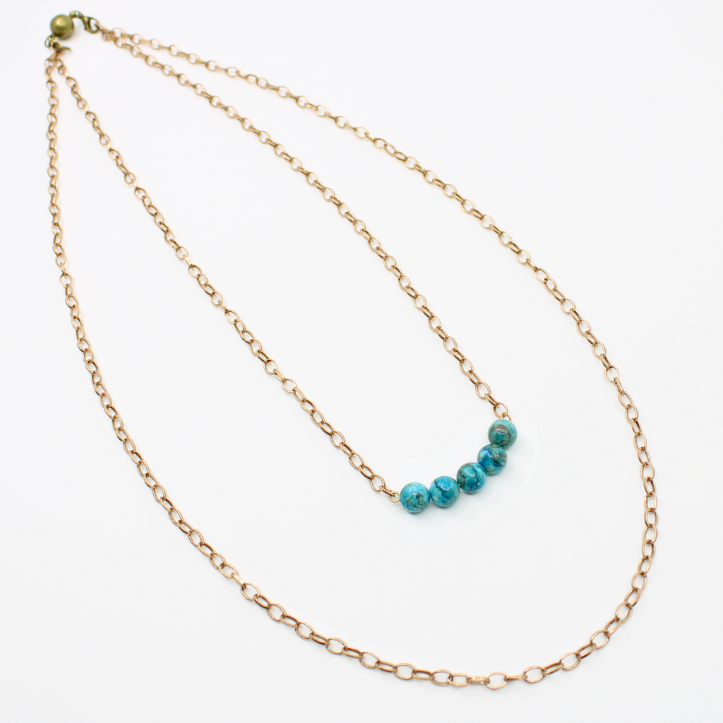 Stainless steel necklace featuring a gold chain with a row of five Aqua Terra Jasper beads, beautifully marbled in blue, set against a pristine white background. Perfect for layering.