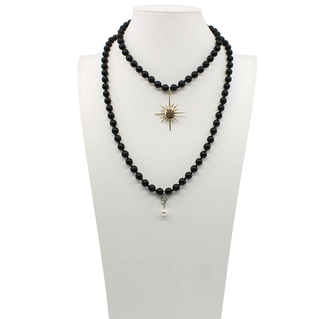 Black onyx necklace with a sunburst pendant reading Its All Good. Gold clasp and pearl accent detail on chain.