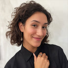 A person wearing small stone drop earrings with a V-shape wire design in a colorless setting.