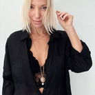 A smiling person with blonde hair wears a black shirt and layered necklaces, including a delicate layering chain adorned with howlite heart beads, against a plain background.