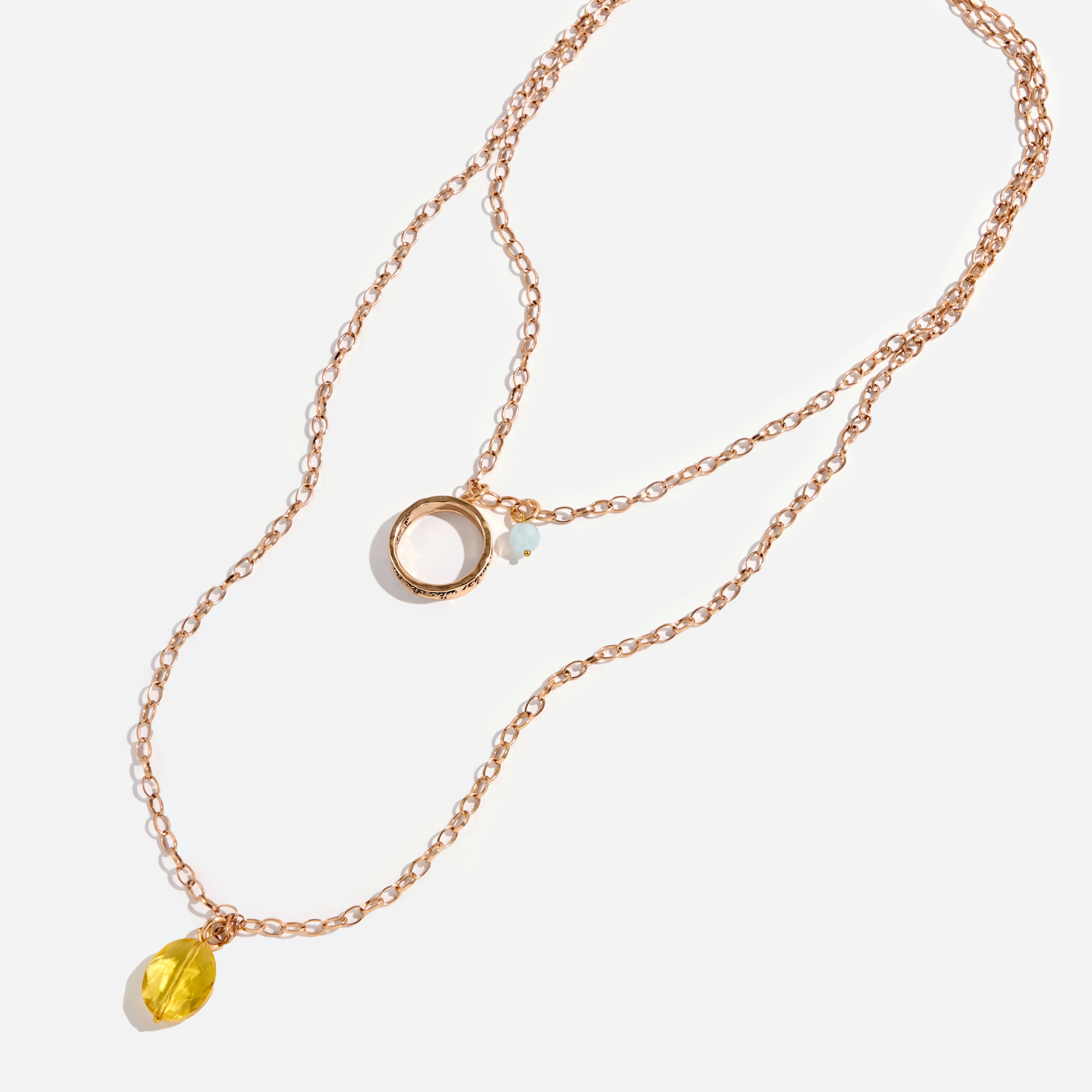 A collection of jewelry including a silver ring with an inscription, a gold necklace with a clear faceted crystal and a rose quartz heart accent, and a silver necklace with a faceted smoky crystal and moonstone accent.