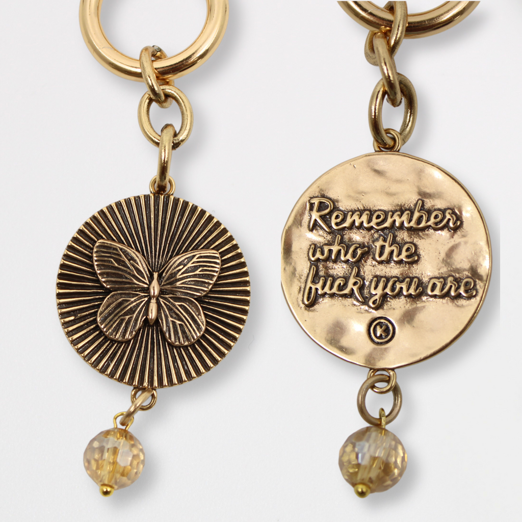 DETAILS AND PRODUCT DISPLAY OF GOLD VARIANT; one with a butterfly pendant and crystal accent, the other boldly inscribed with Remember who the fuck you are.