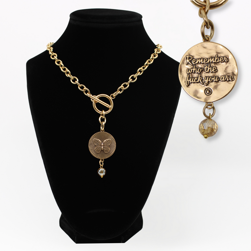 DETAILS AND PRODUCT DISPLAY OF GOLD VARIANT ON BUST; one with a butterfly pendant and crystal accent, the other boldly inscribed with Remember who the fuck you are IN GOLD.