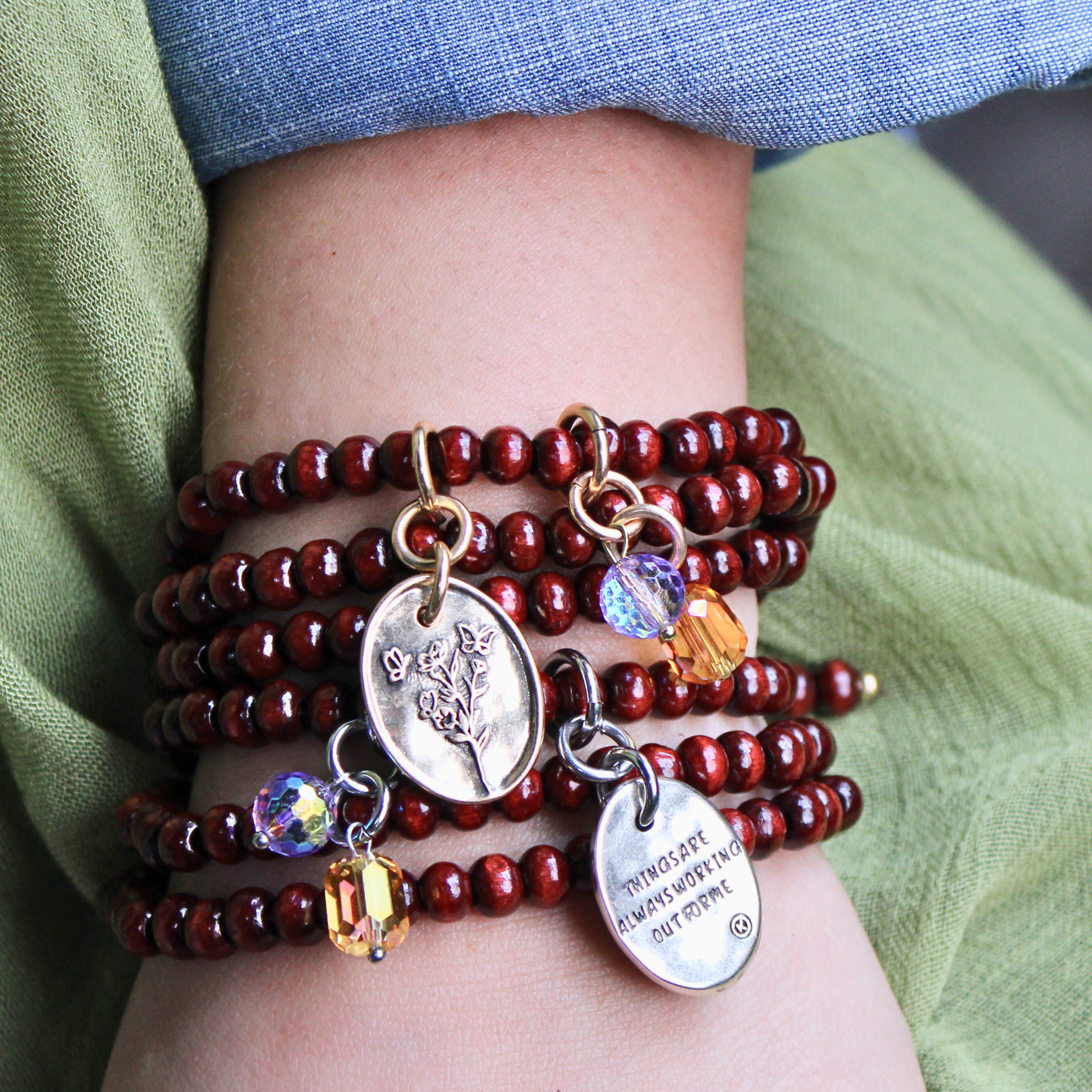 Stack of red beaded bracelets with charms on a wrist, against a green fabric background.