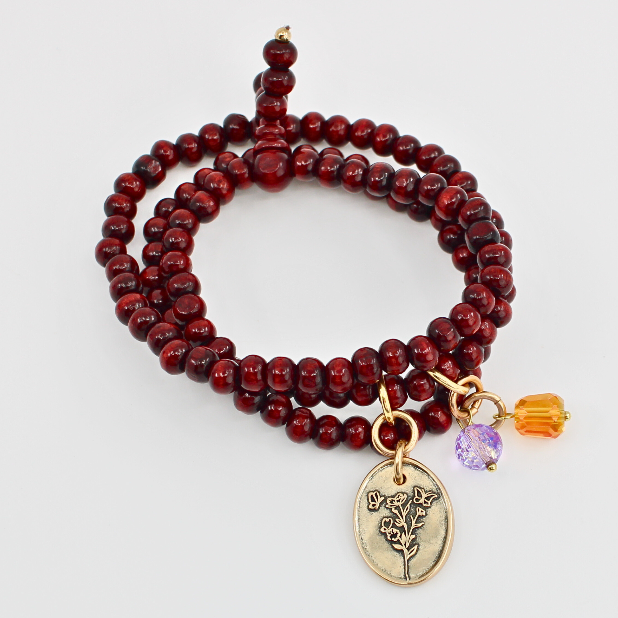 Red beaded bracelet with gold charm and purple bead on a white background