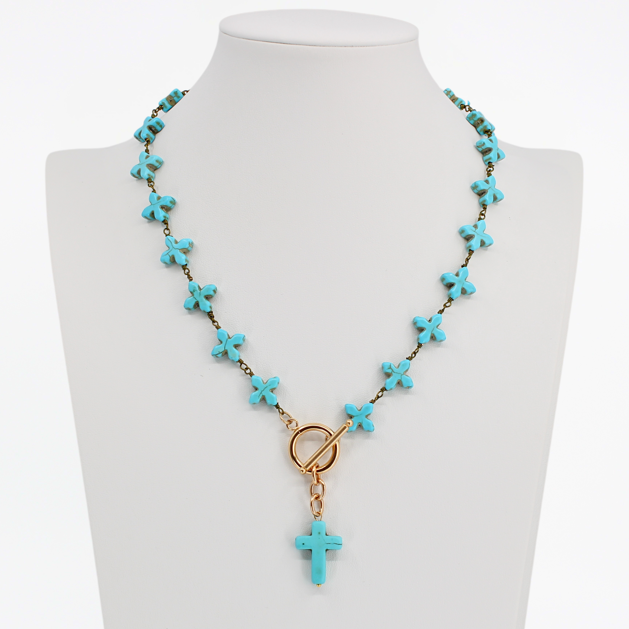Turquoise cross necklace on a mannequin bust against a white background