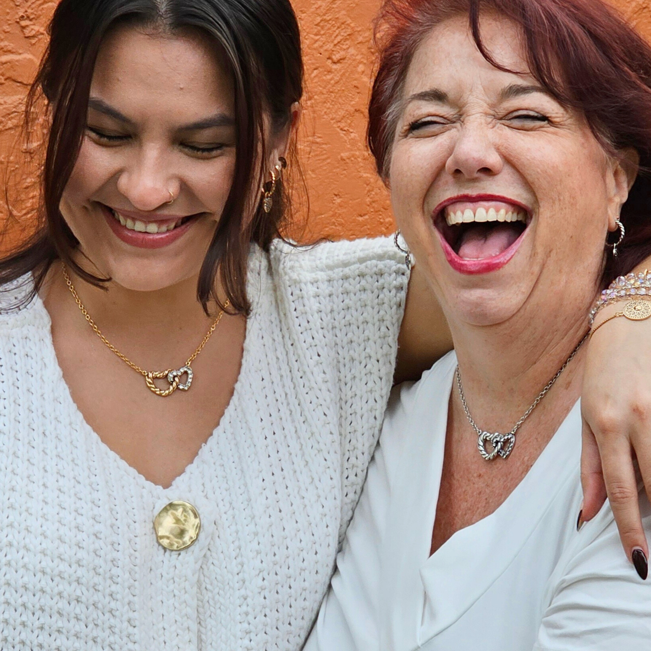 Two women laughing together against an orange wall.
