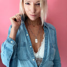 A person wearing a denim shirt and a white lace top, showcasing a silver-colored stainless steel chain necklace with a square pendant.