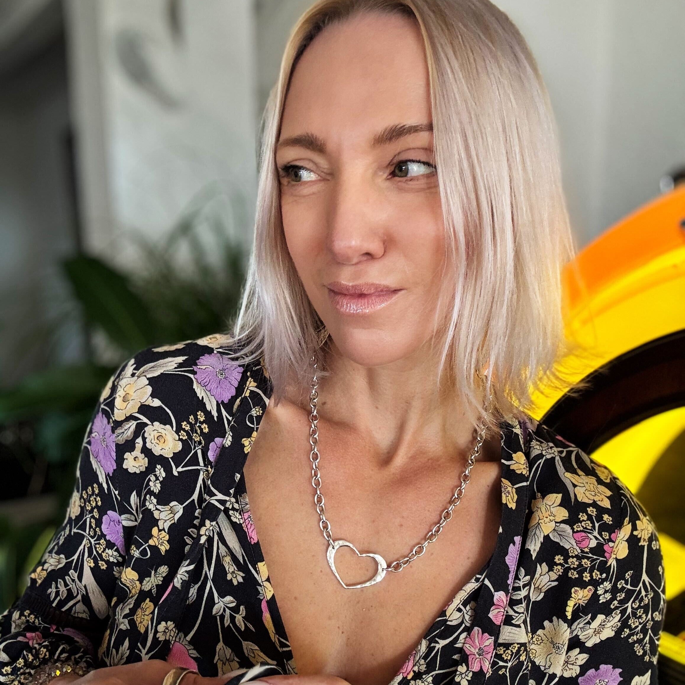 Woman wearing a floral top and heart-shaped necklace with a blurred background
