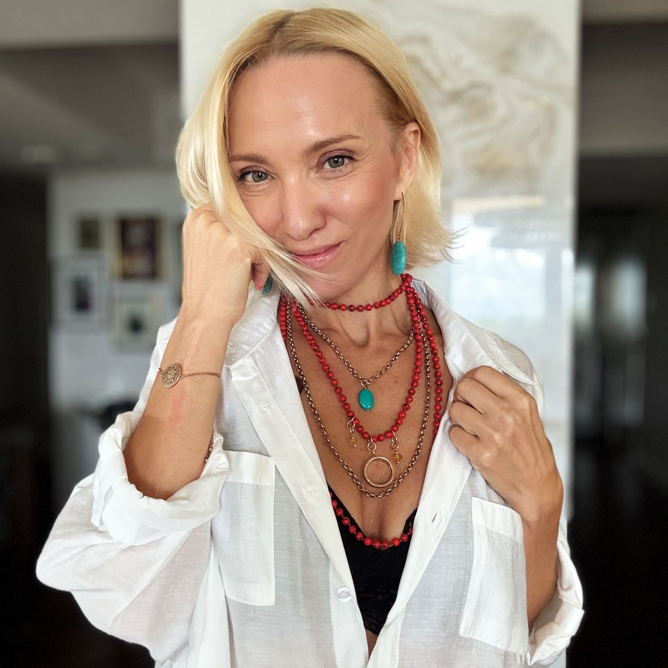 Woman wearing a white shirt and multiple necklaces indoors