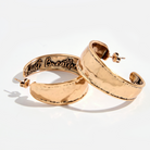 A pair of hoop earrings with a hammered texture, one with 'Just Breathe' inscribed, in silver and gold colors.