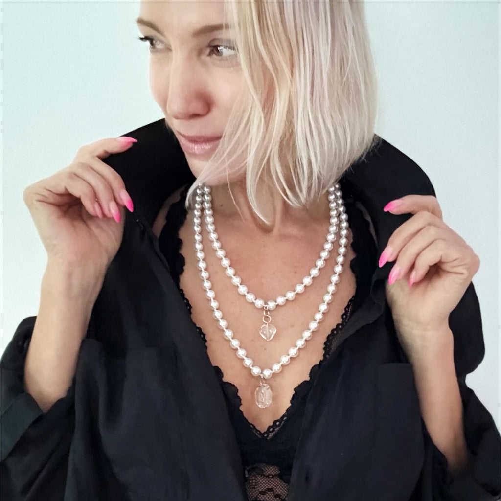 white layering pearl necklace
Strings of white pearls with quartz heart-shaped pendants lie on a light surface. These pearl necklaces are connected to the pendants using metal clasps in gold or silver finish options.