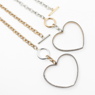 Two exquisite open-heart pendant necklaces grace a white background. One flaunts a gold chain with a smooth heart, while the other showcases a silver chain with a textured heart. These mixed-metal jewelry pieces are elegantly secured with circular clasps.