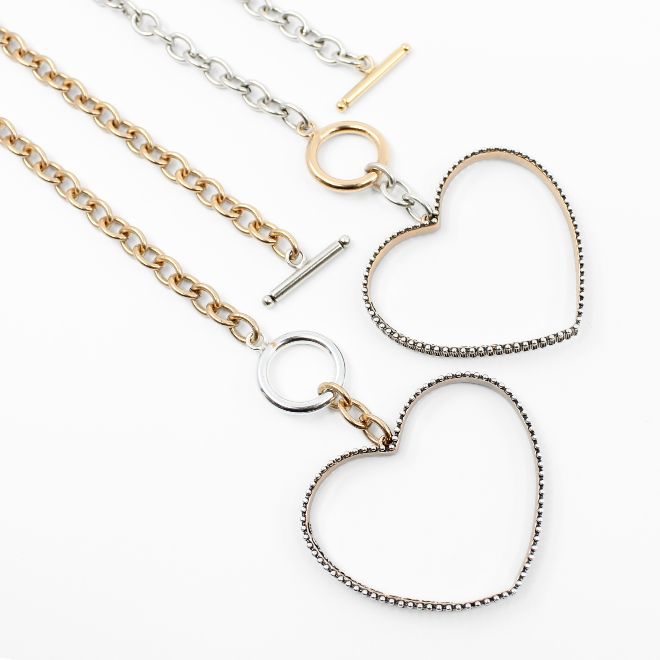 Two exquisite open-heart pendant necklaces grace a white background. One flaunts a gold chain with a smooth heart, while the other showcases a silver chain with a textured heart. These mixed-metal jewelry pieces are elegantly secured with circular clasps.