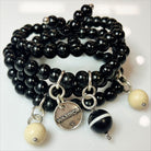 A person's wrist wearing a black wooden Boho wrap bracelet with a silver finish pendant and river stone accents.