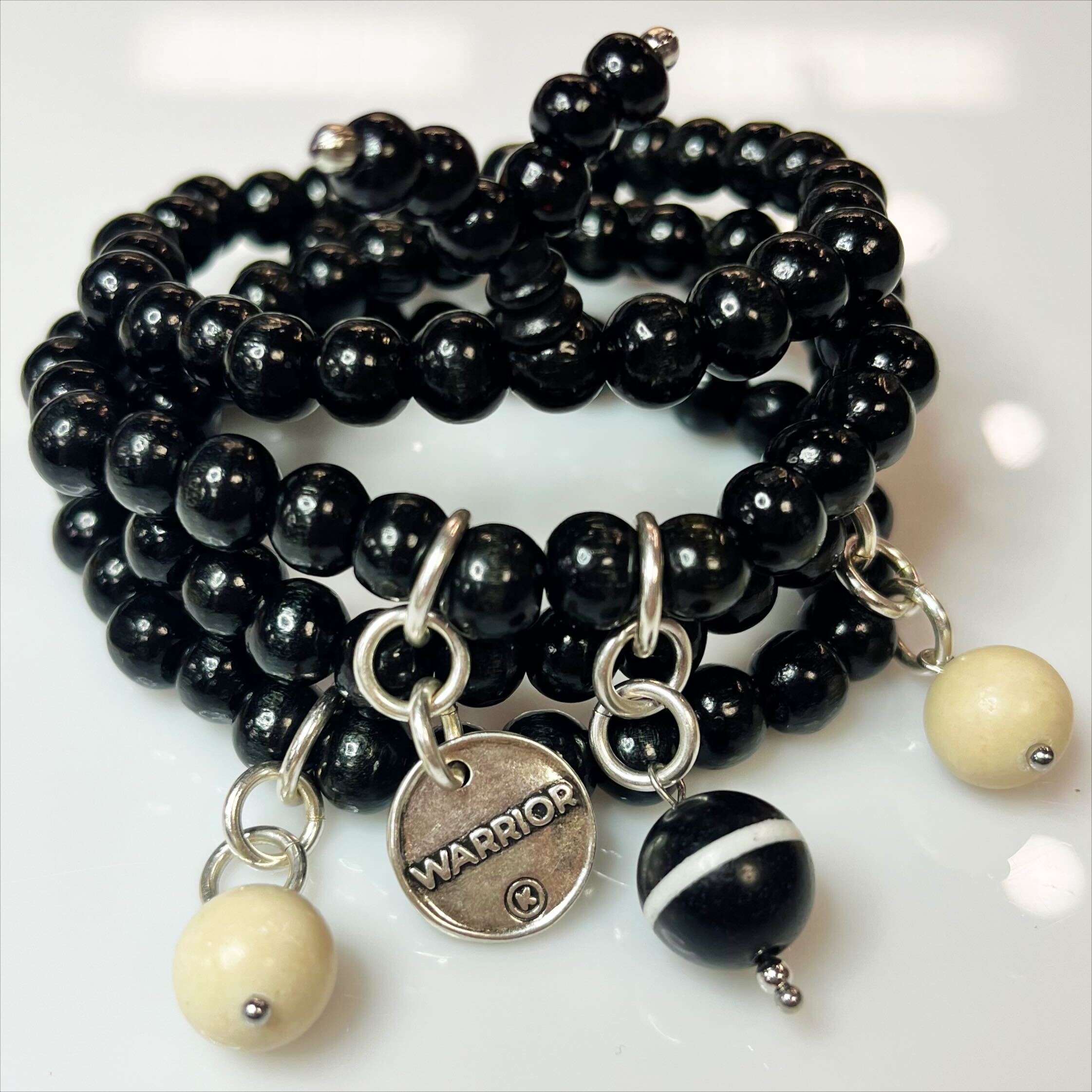 A person's wrist wearing a black wooden Boho wrap bracelet with a silver finish pendant and river stone accents.