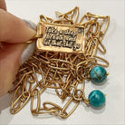 A brass necklace with a paperclip chain design, featuring a rectangular pendant with a heart cut-out and two magnesite accent stones on a white background.