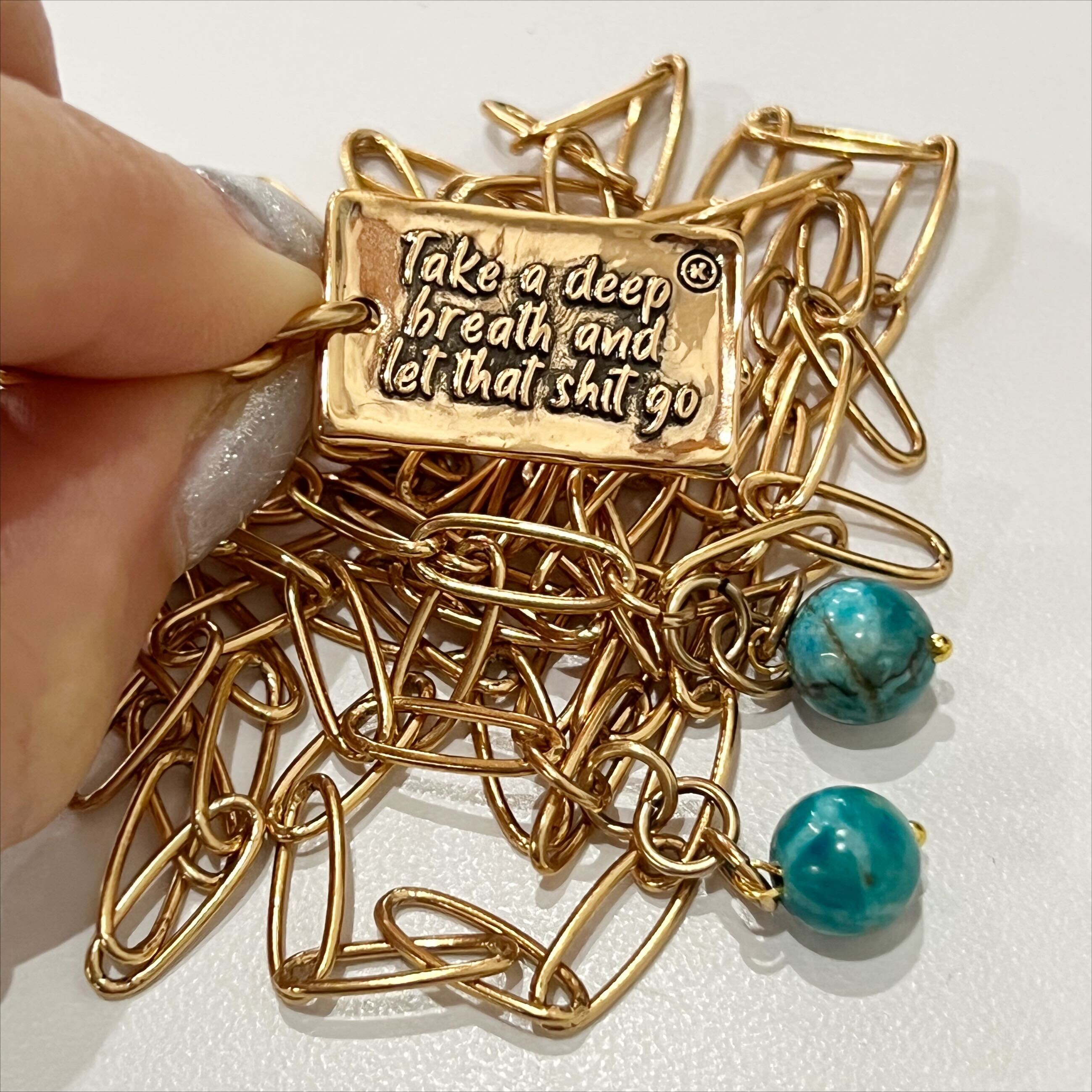 A brass necklace with a paperclip chain design, featuring a rectangular pendant with a heart cut-out and two magnesite accent stones on a white background.