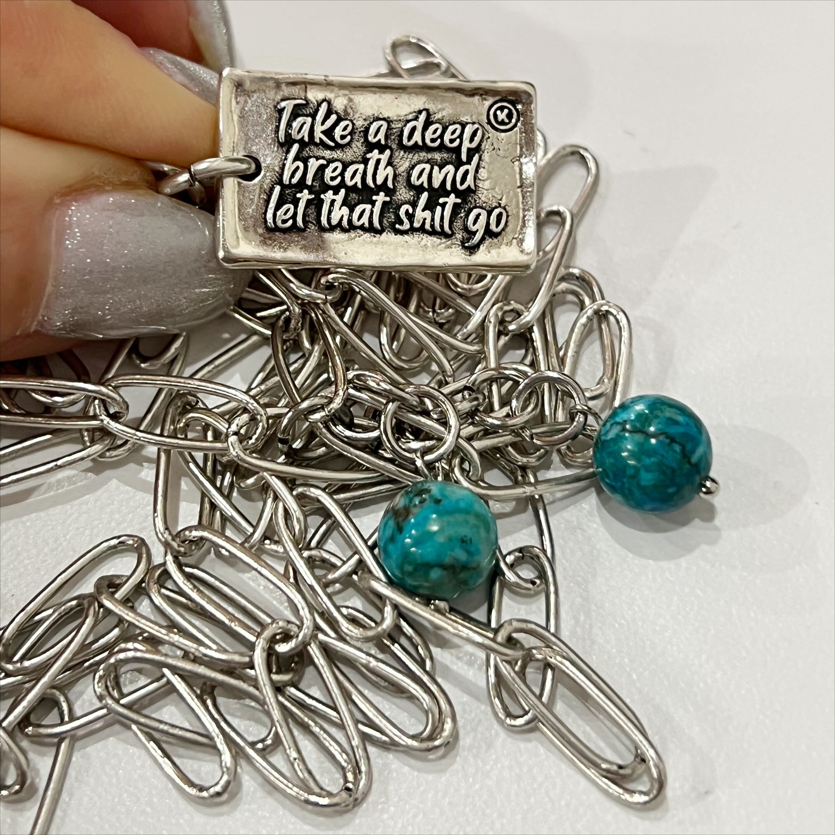 A brass necklace with a paperclip chain design, featuring a rectangular pendant with a heart cut-out and two magnesite accent stones on a white background.