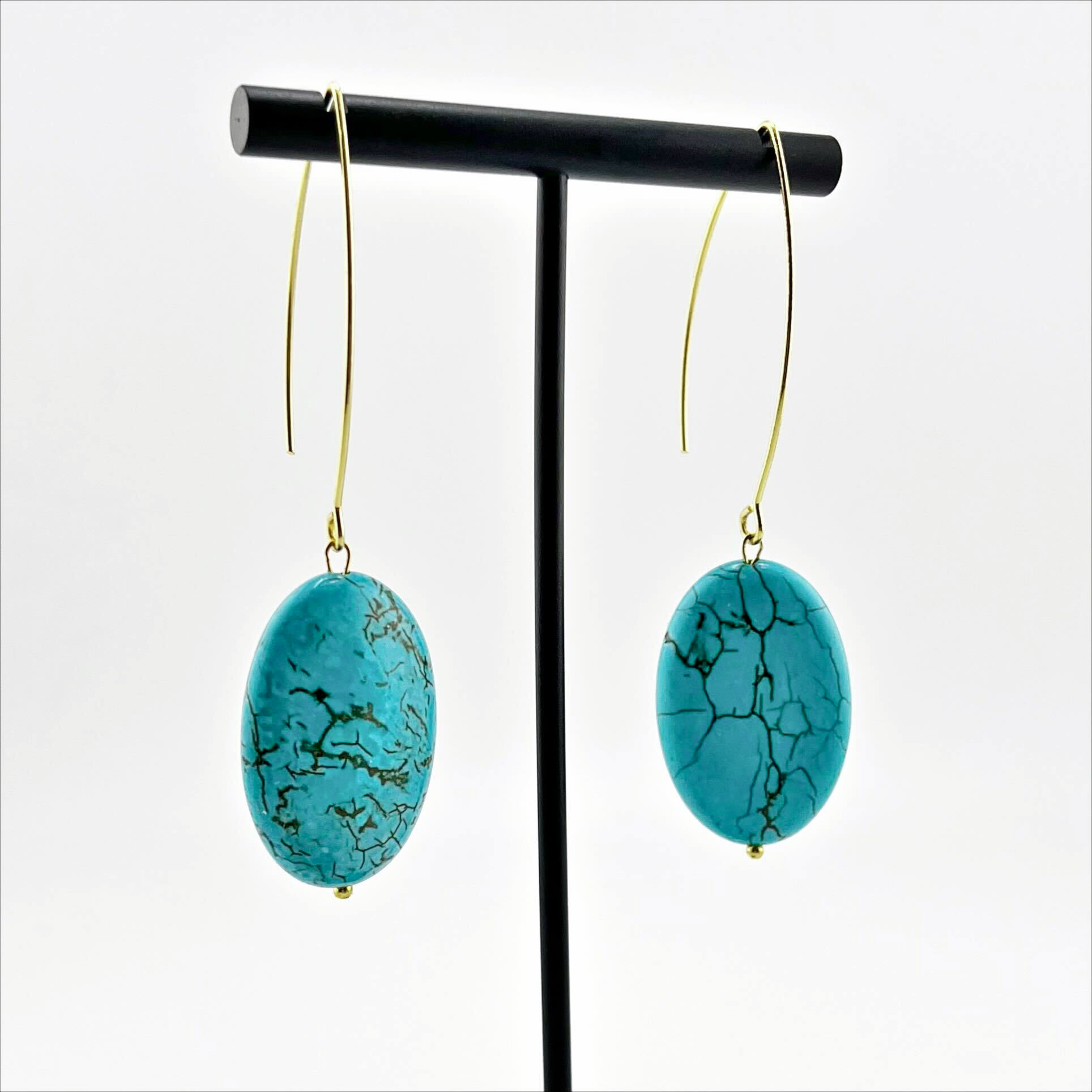 A person wearing large stone drop earrings with a V-shape wire earring holder.