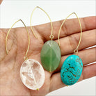 Three stone drop earrings in gold finish, each with a different color of stone: clear quartz, green aventurine, and blue howlite, held in a person's hand.