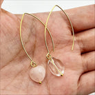 A pair of threader earrings with gold finish and heart-shaped stones, displayed on a hand.