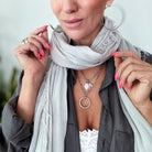 A person wearing a silver finish necklace with a clear iridescent crystal and pearl star, along with a grey shirt and a light grey scarf.