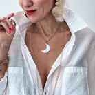 A person wearing a white shirt and showcasing a silver-colored moon-layering chain necklace with a pearl moon shell accent and a magnetic clasp.