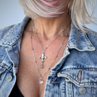Person wearing a denim jacket with layered necklaces featuring a fleur-de-lis pendant.