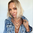 Woman wearing a denim jacket with layered necklaces against a plain background