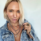 Woman wearing a denim jacket with layered necklaces and a key-shaped pendant.